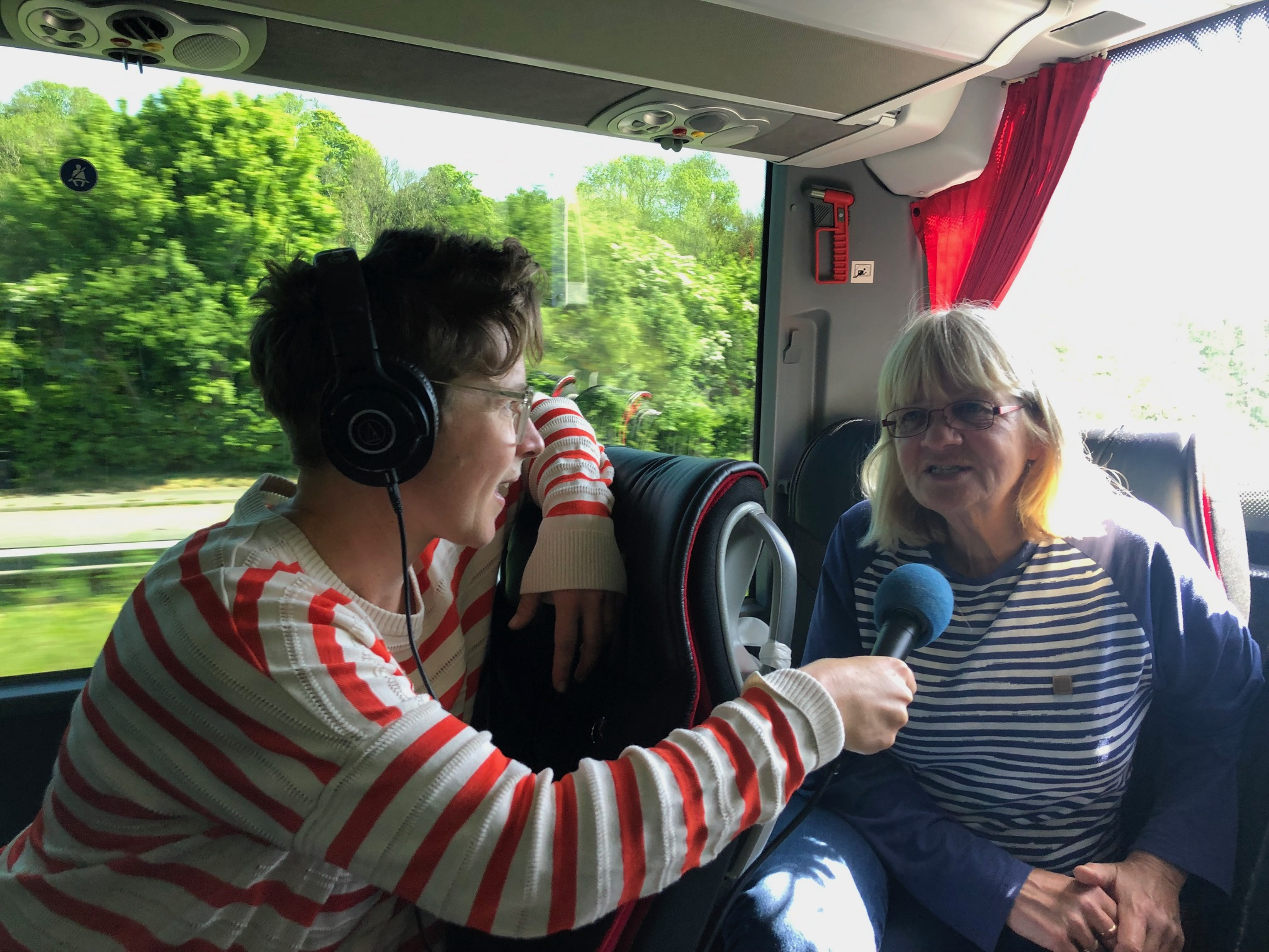 Charlotte is wearing headphones and holding a microphone whilst interviewing a female pioneer football player on a coach