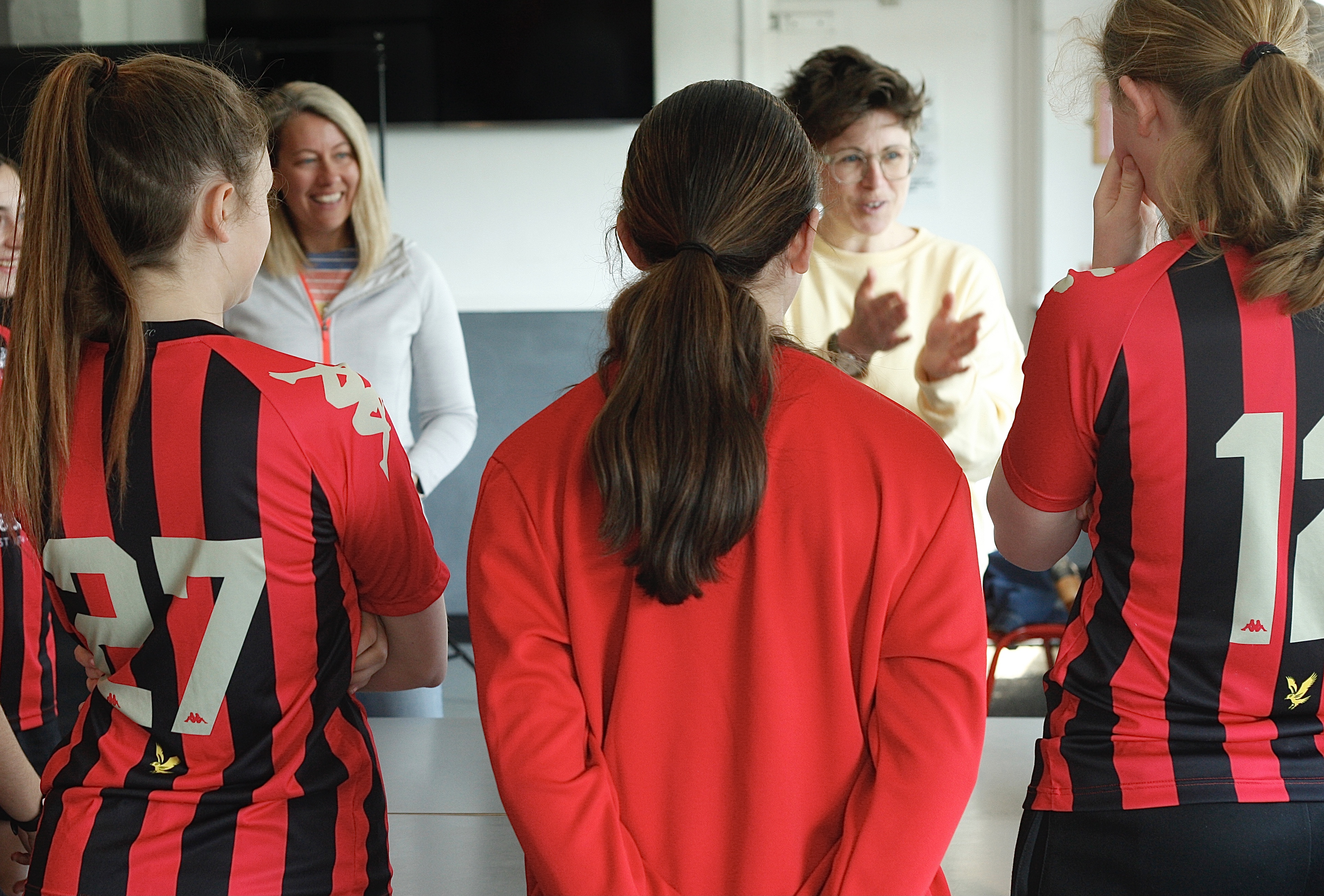 Jody and Charlotte are talking and laughing with a team of young female football players