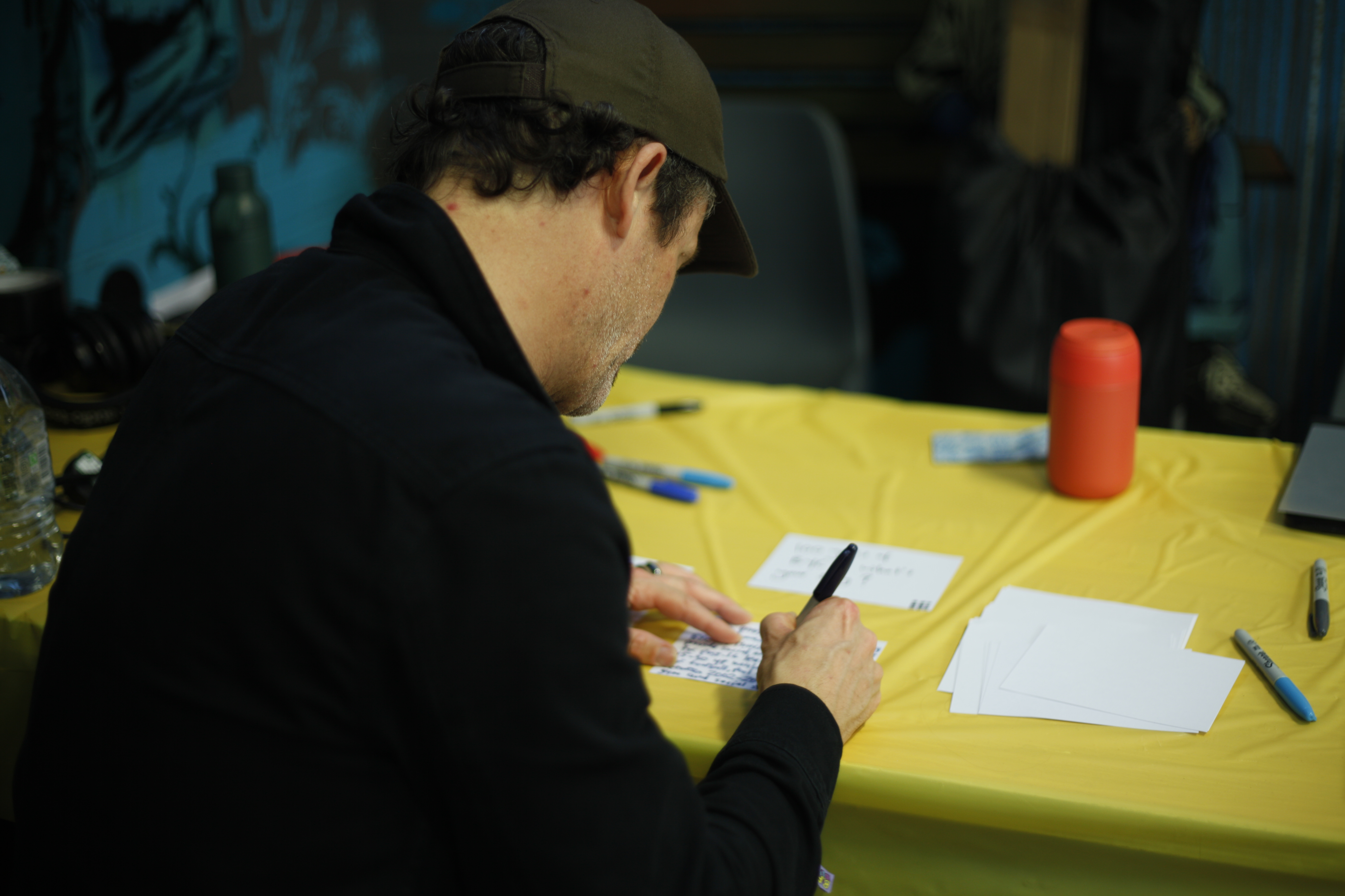 A man is sitting down at a table covered in a yellow table cloth to fill in a comments card